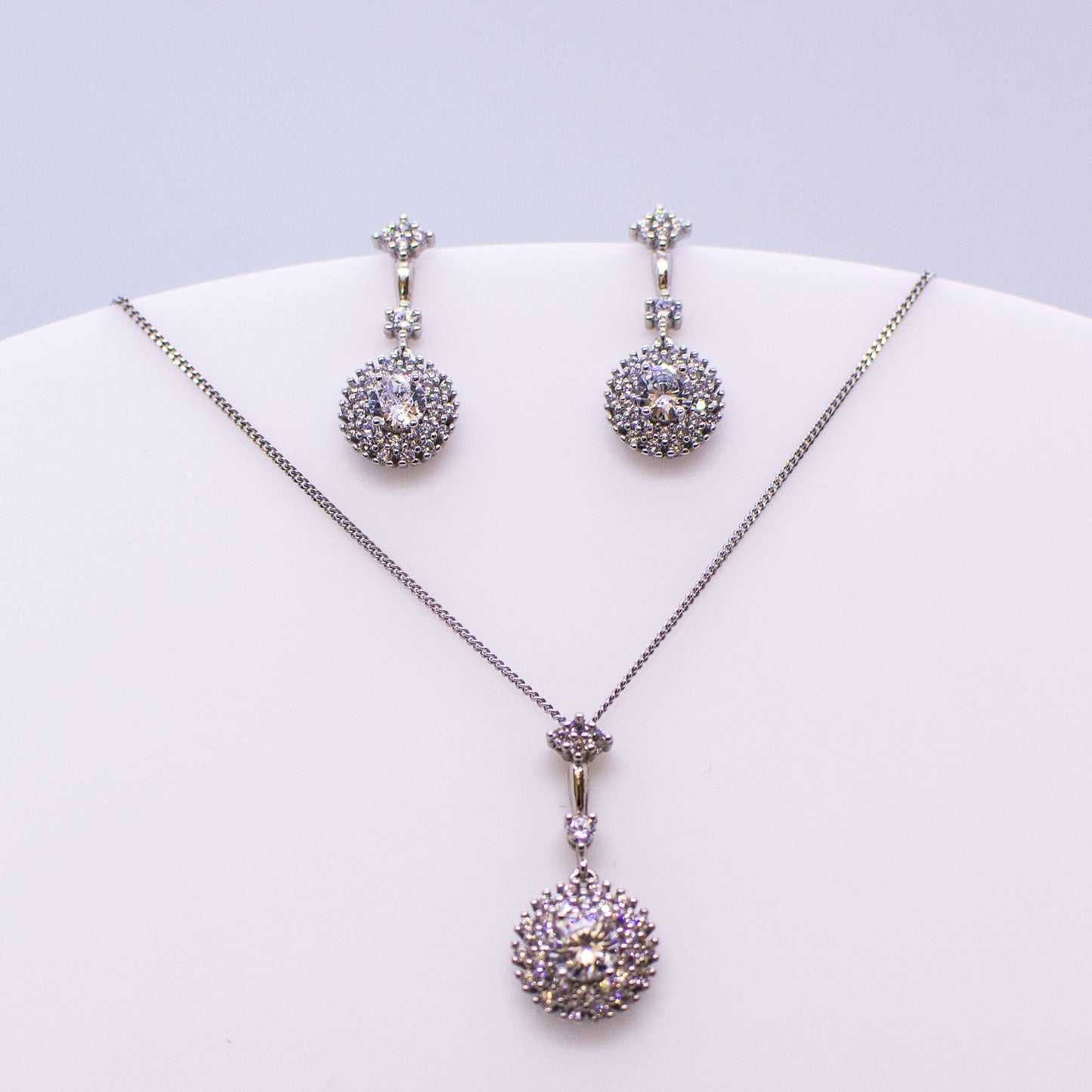 These sterling silver round shaped drop earrings set with glittering cubic zirconia stones with a double halo accompanied by the matching necklace are the perfect addition to any outfit. Product details: Product materials: 925 sterling silver, cubic zirconia Chain length: 44cm fine diamond cut curb chain Pendant dimensions: 26mm L x 12mm W Earring dimensions: 24mm L x 10mm W Drop earrings with stud wires and butterfly backs.