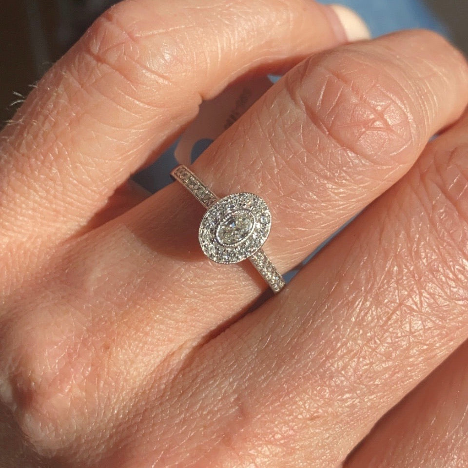 This oval cluster diamond engagement ring is a complete classic. Its simplicity is so romantic. The Details... One 9ct white gold diamond engagement ring. Diamond halo cluster in an oval shape with pavé diamond-set shoulders. 0.34ct in total of diamonds. Colour H, Clarity SI Centre stone: 0.16ct Melée: 0.18ct 9ct white gold. Size N.