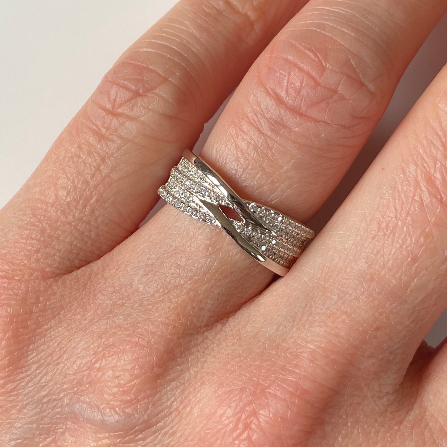 Silver CZ crossover ring by NJO featuring intertwined bands and sparkling cubic zirconia accents.