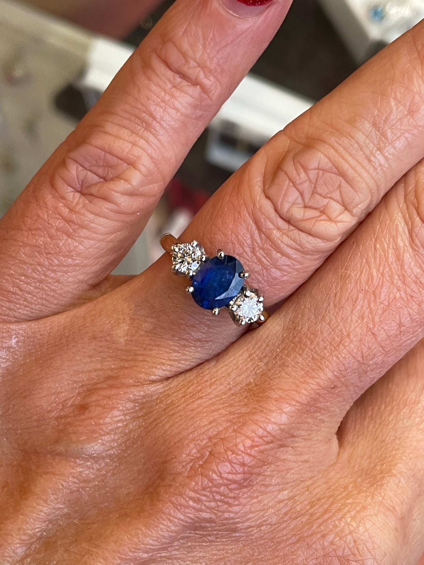 18ct gold sapphire and diamond engagement ring by John Michael featuring a central blue sapphire with sparkling diamonds.