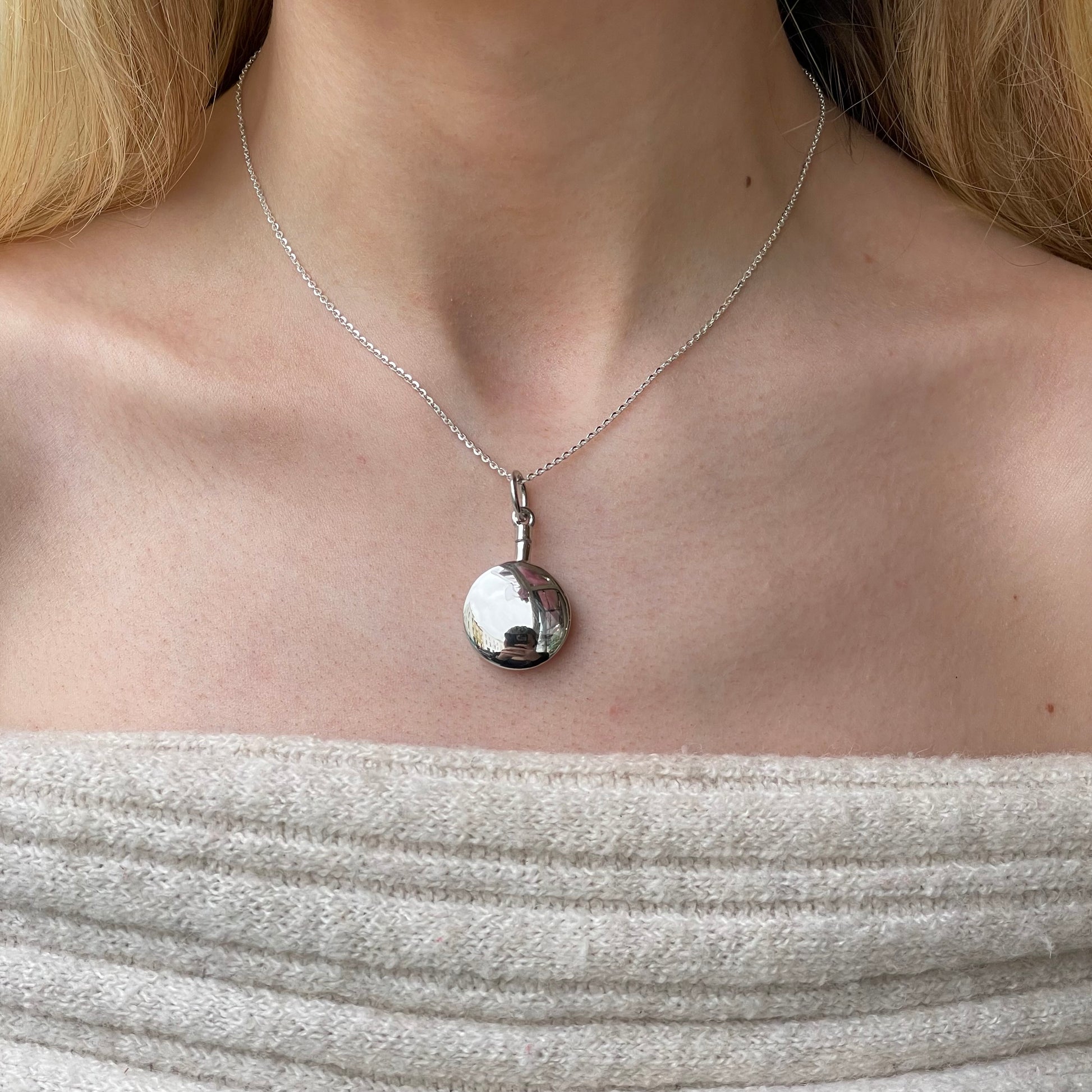 Silver round ash locket necklace by Insignia, featuring a polished circular pendant with a secure clasp and intricate detailing.