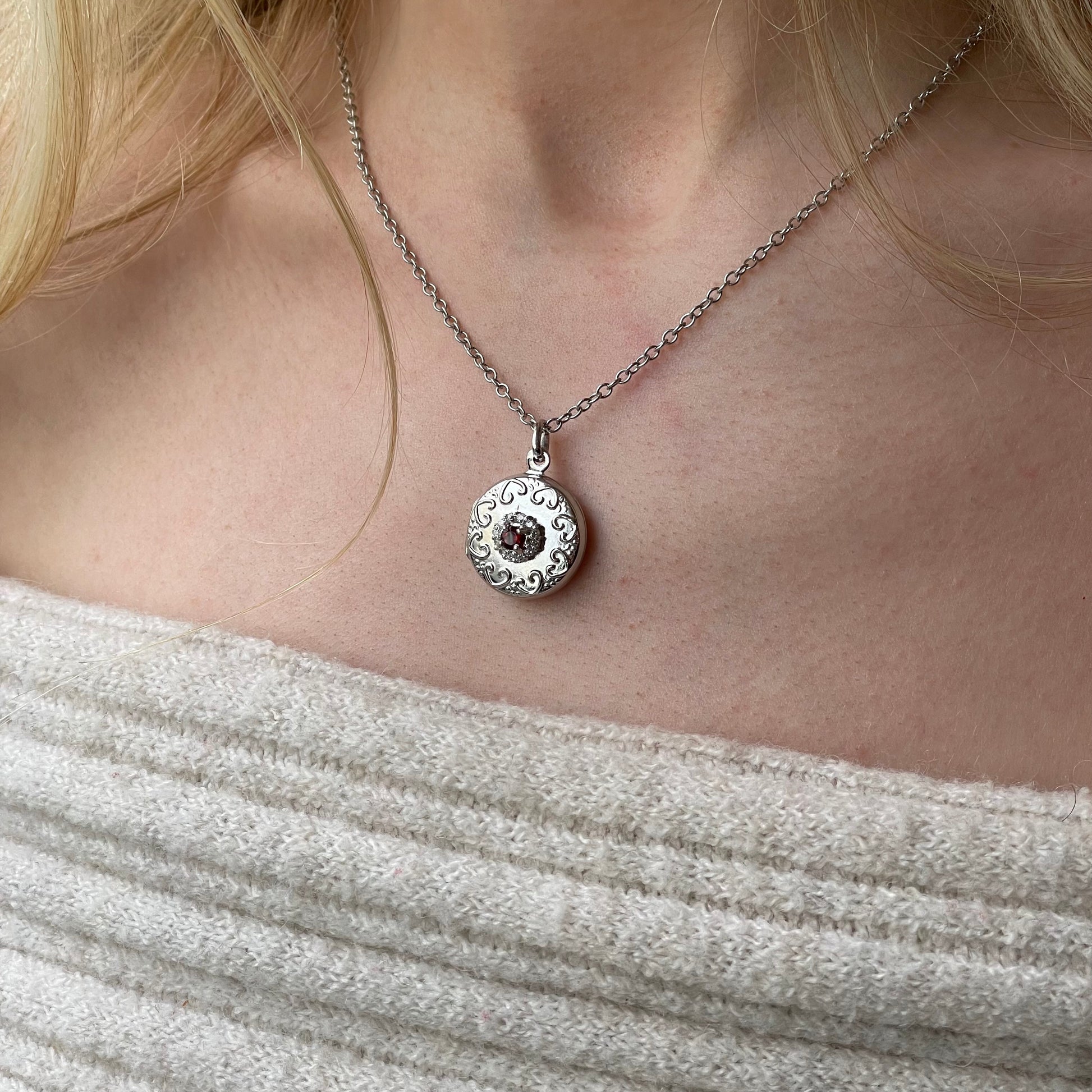 Silver round garnet and CZ embossed locket necklace with chain, featuring intricate design and polished finish.
