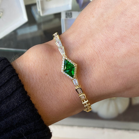 Gold bracelet with a green gemstone on a wrist, blurred background