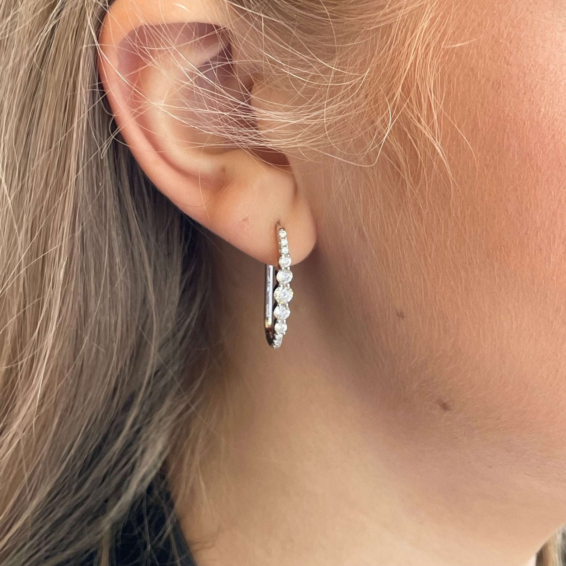 Silver elongated CZ huggie hoop earrings by Comero, featuring sparkling cubic zirconia stones and a sleek hoop design.