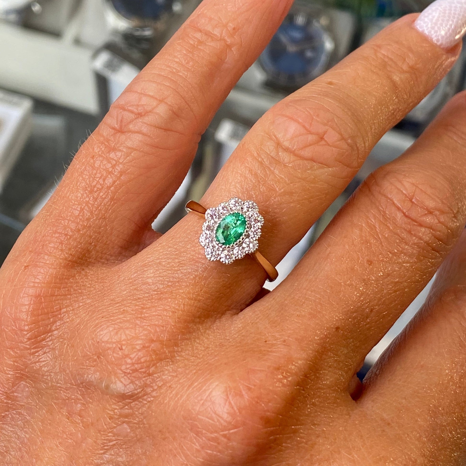 Close-up of a hand wearing a ring with a emerald gemstone, blurred background