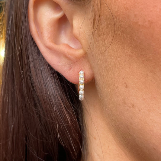 Comero Sunshine Pearl Huggie Hoop Earrings showing gold hoops with small pearl accents, close-up view of the jewelry.