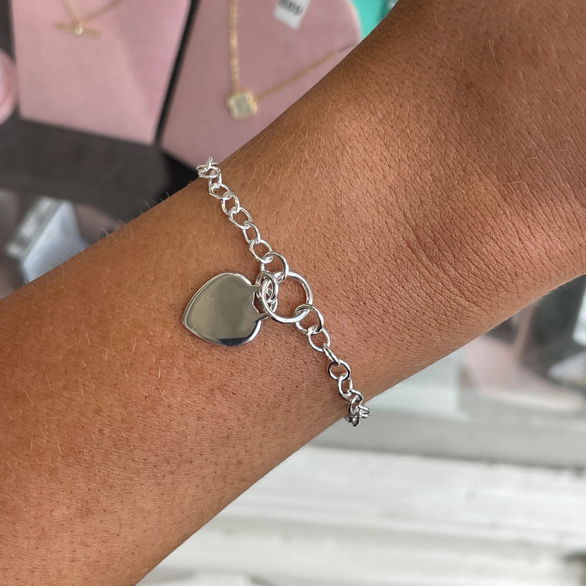 Silver heart disc charm bracelet by CME featuring a delicate chain and heart-shaped pendant on a white background.