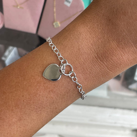 Silver heart disc charm bracelet by CME featuring a delicate chain and heart-shaped pendant on a white background.