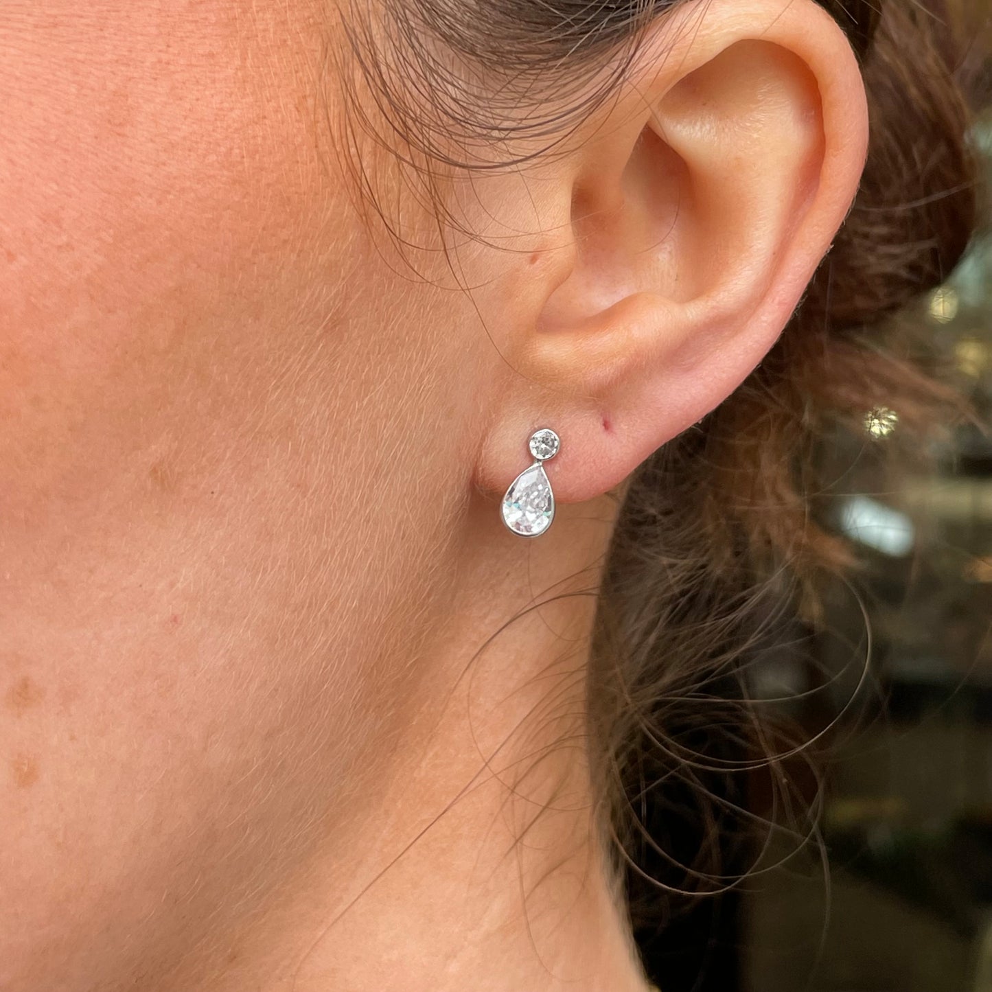 Mark Milton 9ct white gold pear and round cubic zirconia stud earrings with rubover setting, close-up of sparkling jewelry.