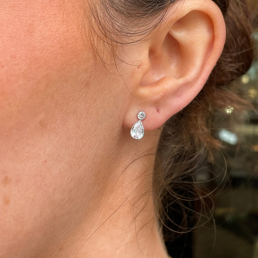 Mark Milton 9ct white gold pear and round cubic zirconia stud earrings with rubover setting, close-up of sparkling jewelry.