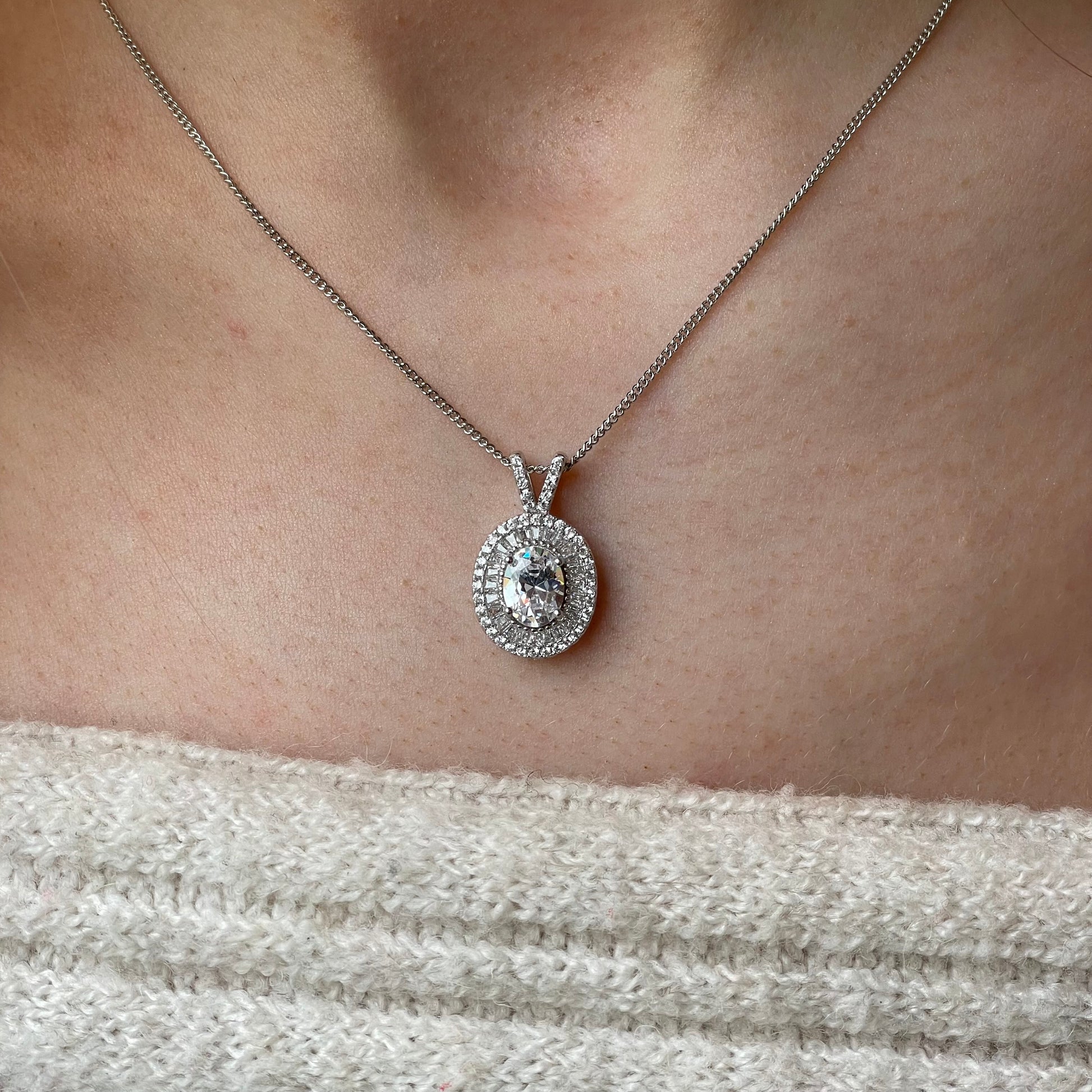 Silver oval CZ halo necklace with a central gemstone surrounded by smaller stones, crafted by Insignia.