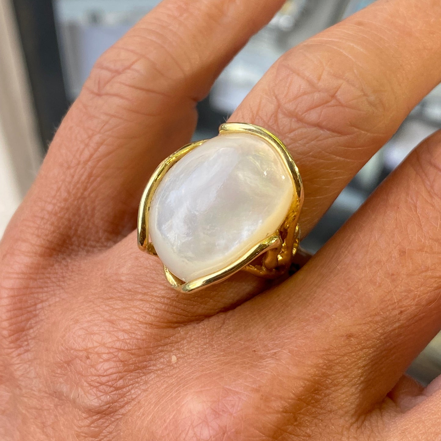 Gold ring with a large piece of mother of pearl on a person's finger
