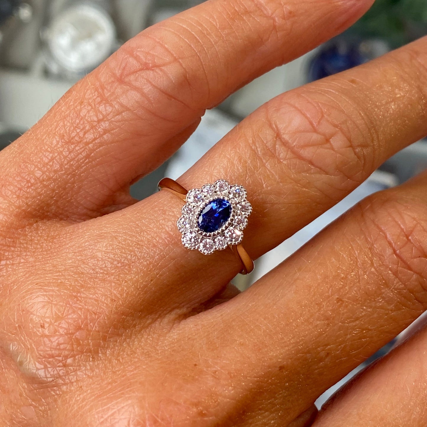 Close-up of a hand wearing a ring with a sapphire gemstone on a blurred jewelry store background