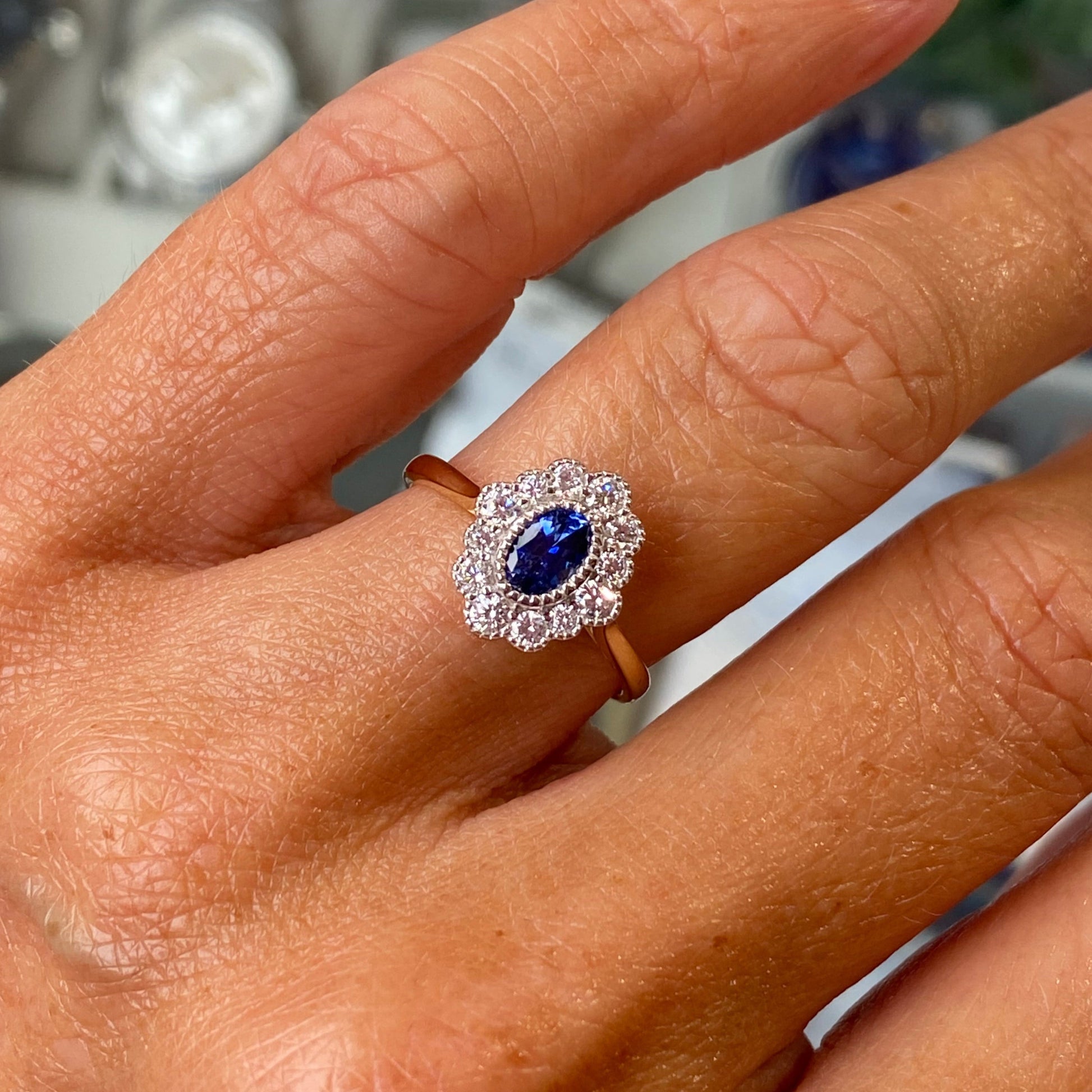 Close-up of a hand wearing a ring with a sapphire gemstone on a blurred jewelry store background