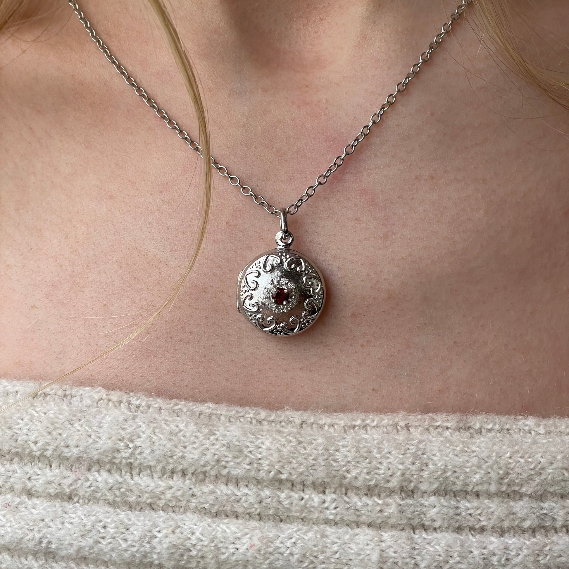 Silver round garnet and CZ embossed locket necklace with chain, featuring intricate design and gemstone accents.