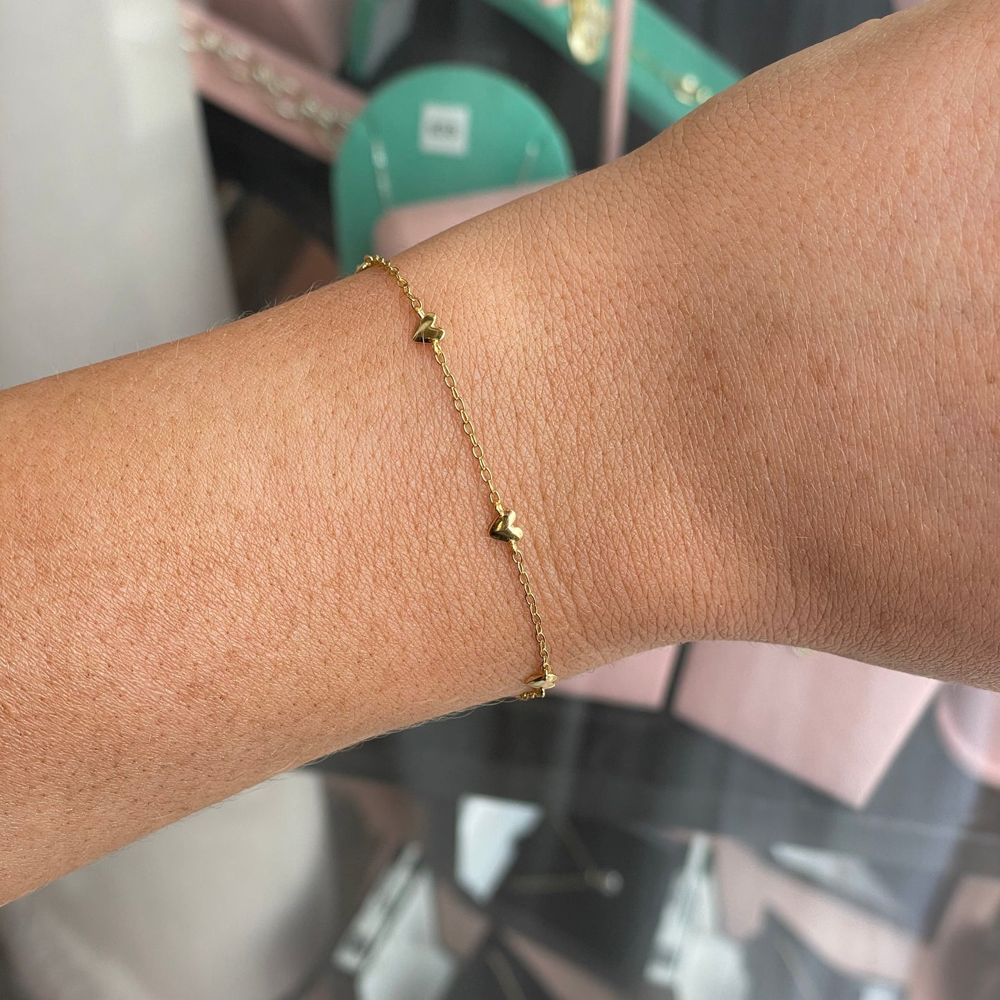 CME Sunshine Six Hearts bracelet featuring gold-tone chain with six heart charms on a white background.