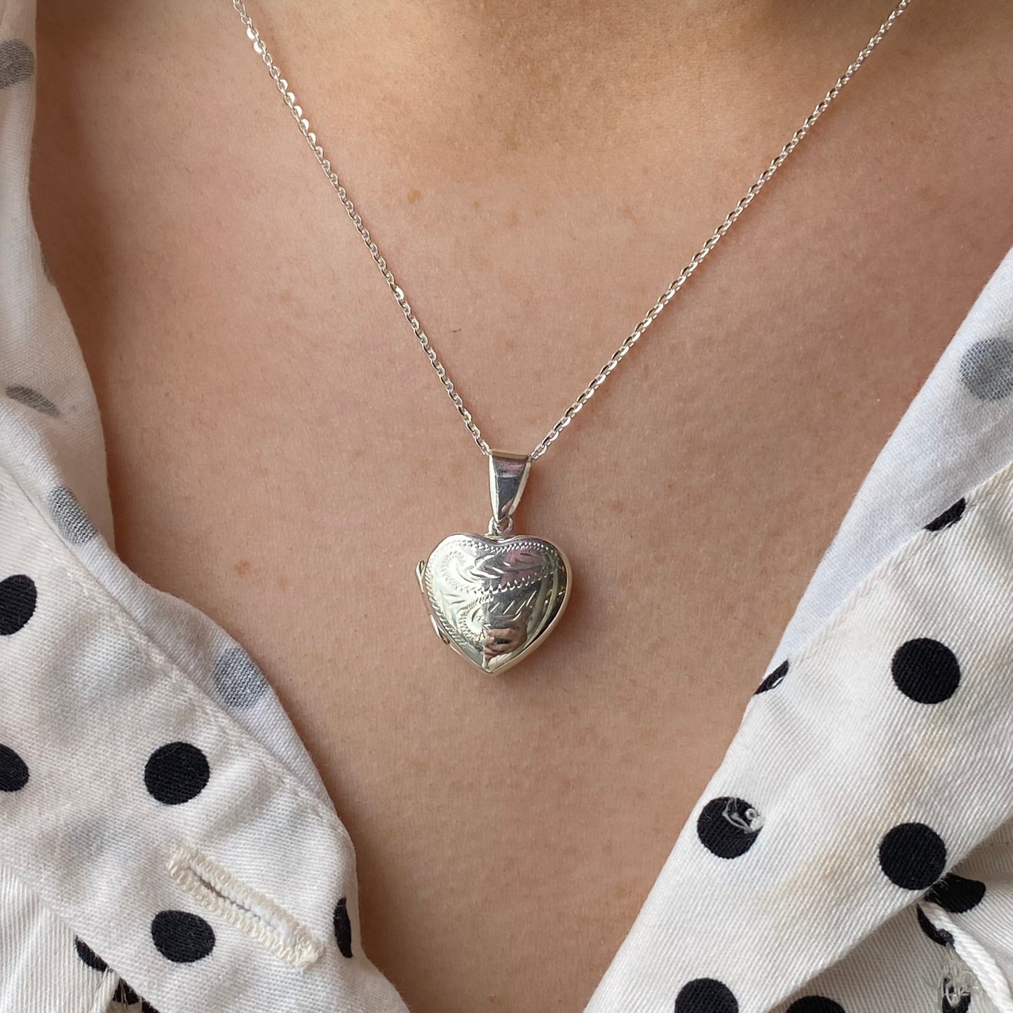 Silver hand-engraved heart locket necklace by THC, showcasing detailed floral design on a polished silver chain.