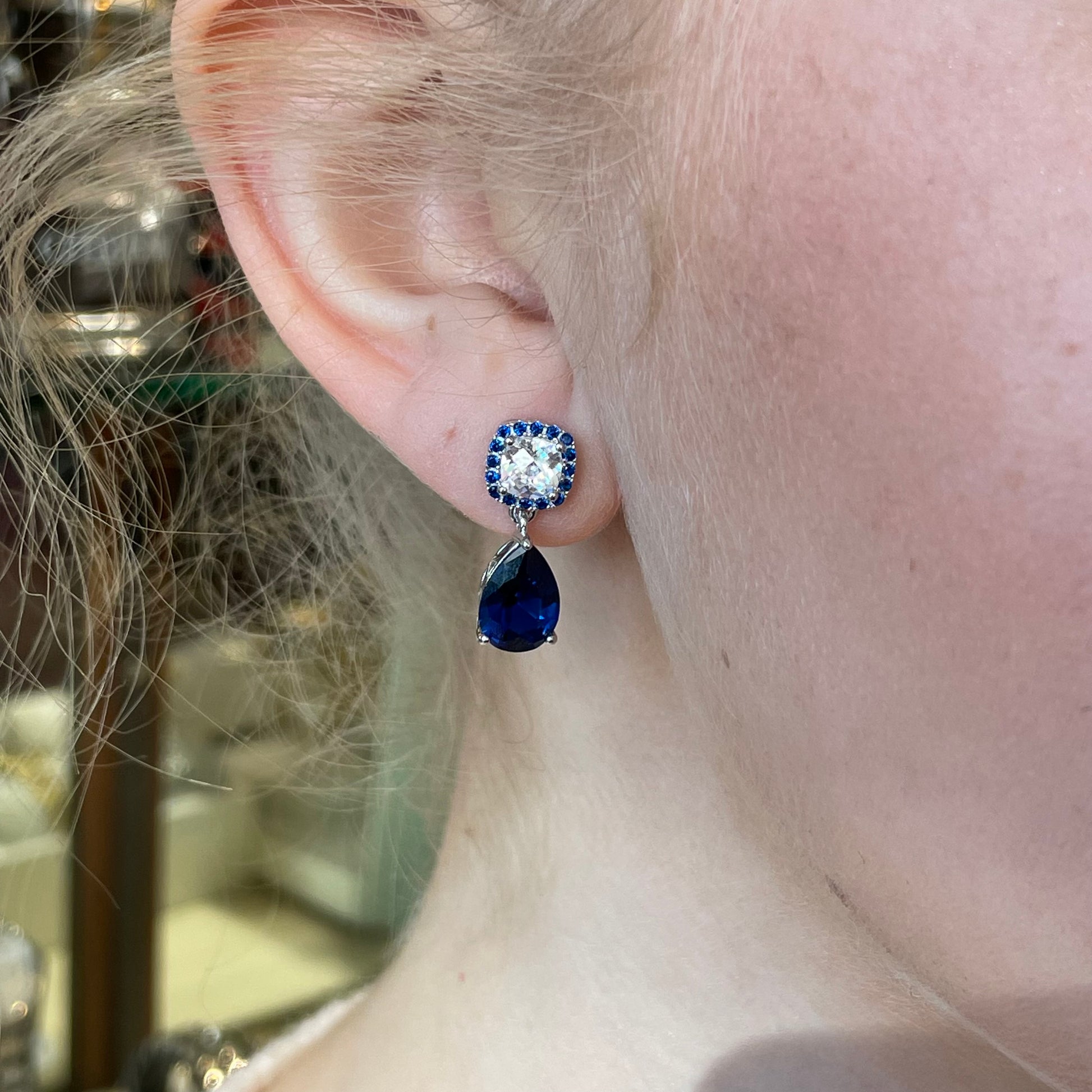 Silver sapphire blue pear-shaped CZ drop earrings by Comero featuring elegant dangle design and sparkling gemstone accents.