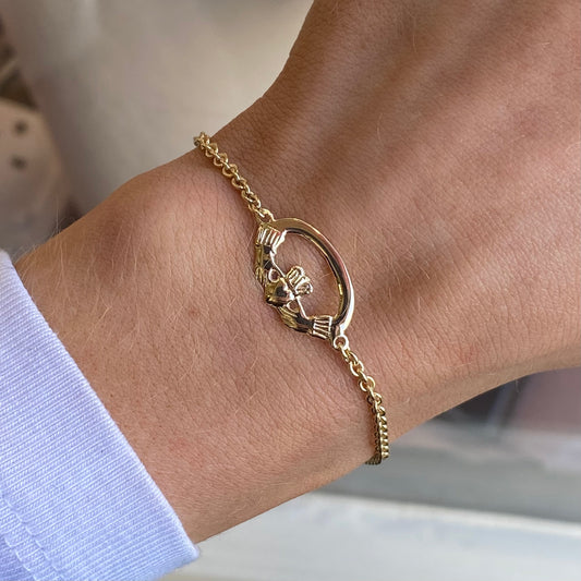 Facet 10ct gold Claddagh bracelet with green stone, featuring intricate heart and crown design on a delicate jewelry piece.