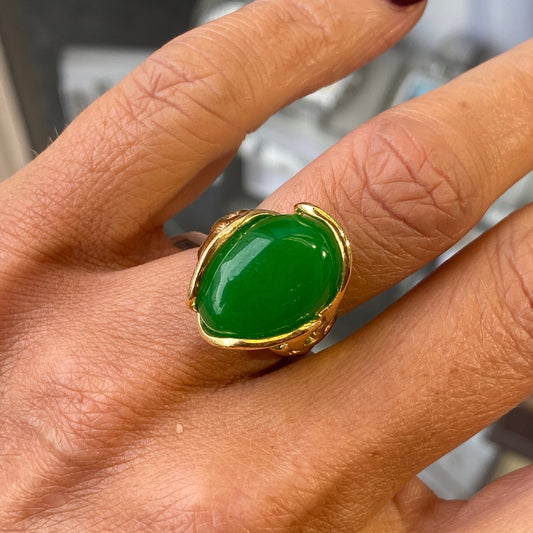 Hand wearing a jade green ring with gold band on a blurred background