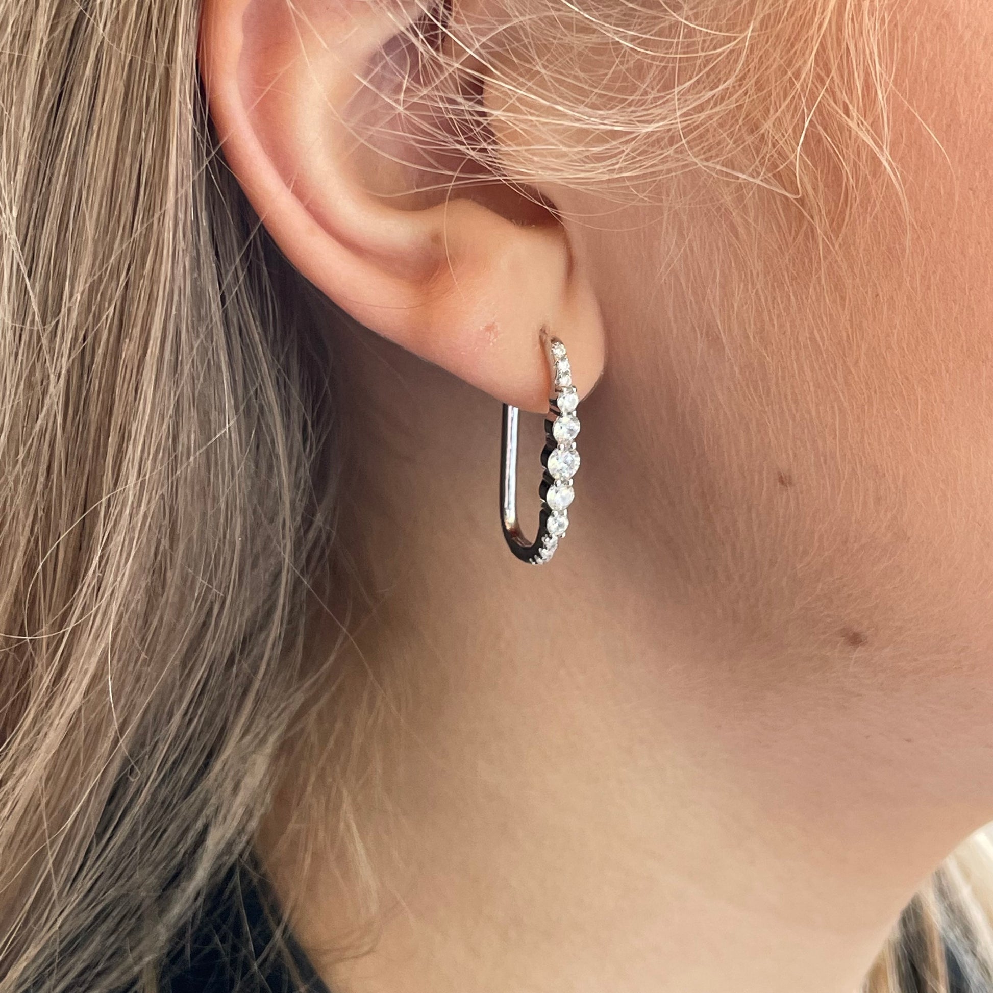 Silver elongated CZ huggie hoop earrings by Comero, featuring sparkling cubic zirconia stones and sleek hoop design.