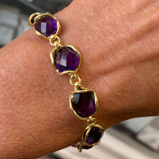Gold bracelet with purple gemstones on a wrist against a blurred background