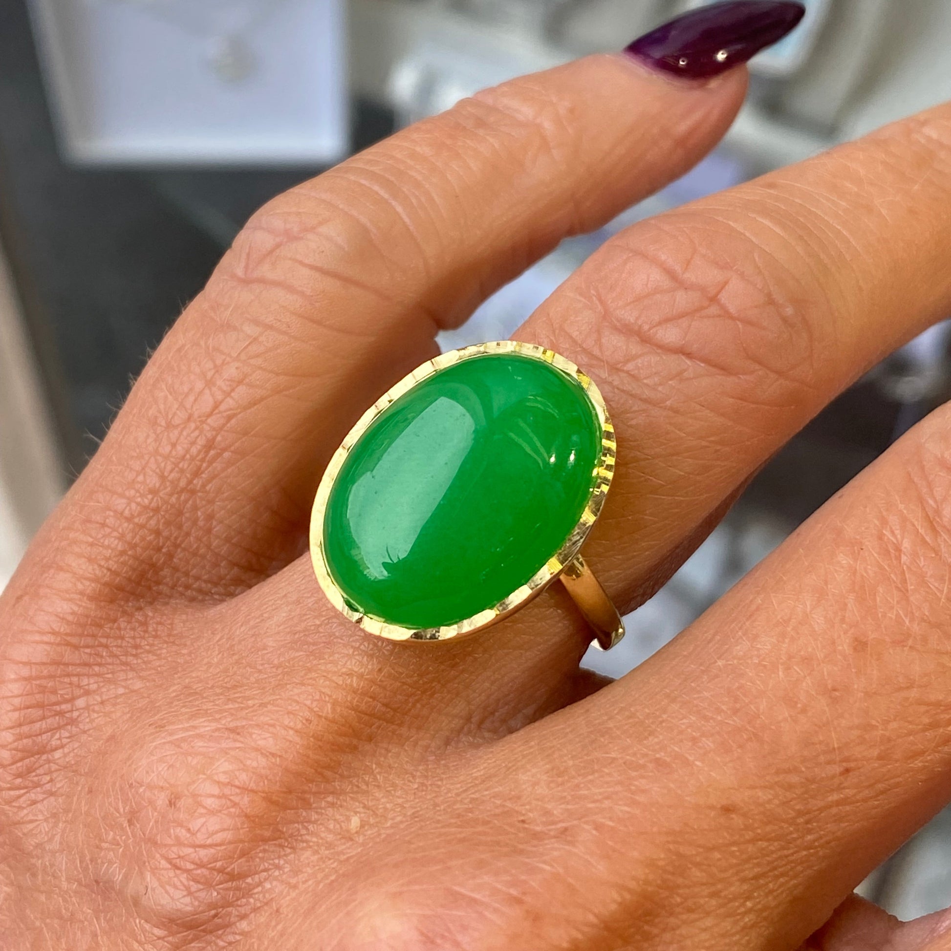 Hand wearing a jade green ring with gold band on a blurred background