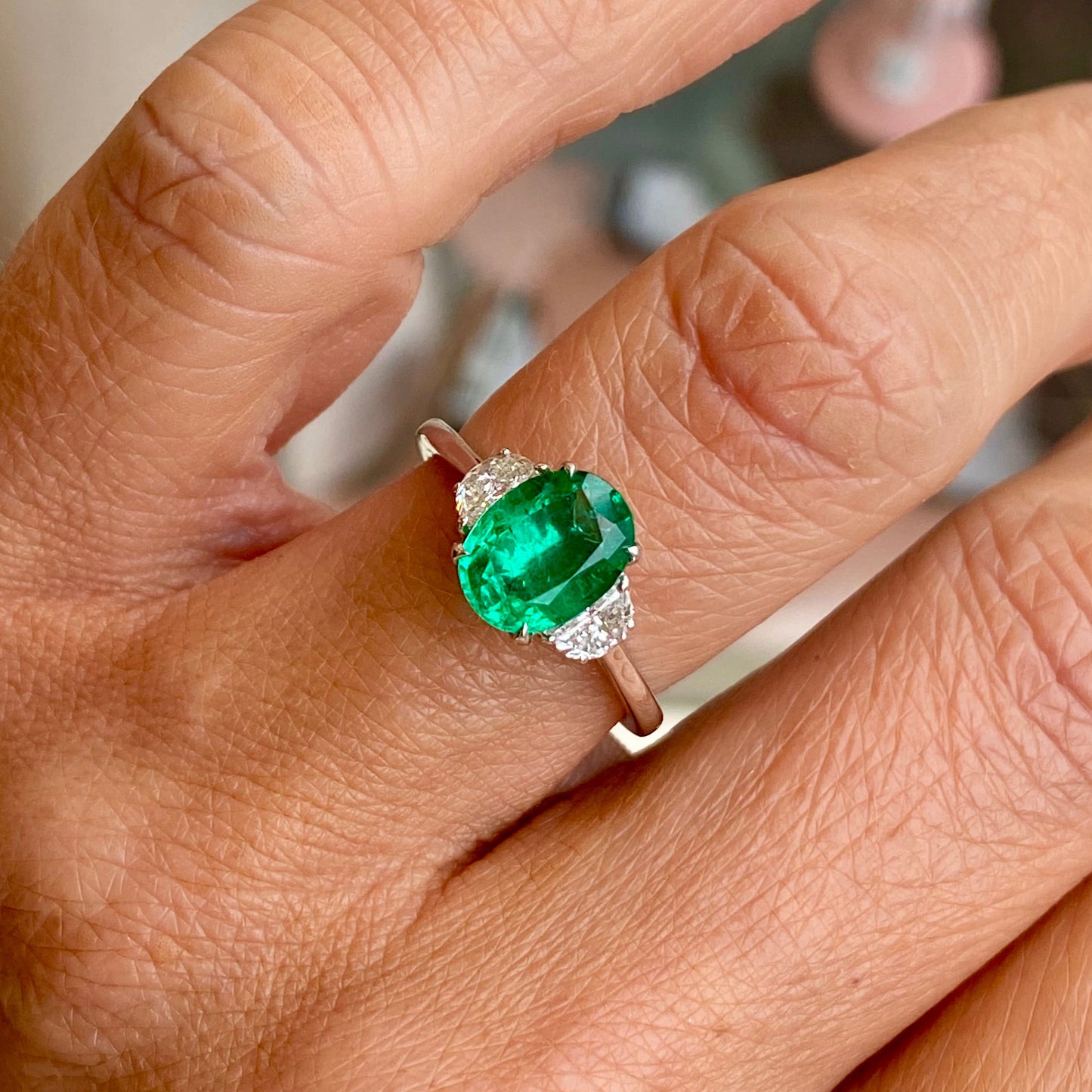 Herbert platinum emerald and diamond ring featuring a central emerald gemstone surrounded by sparkling diamonds.