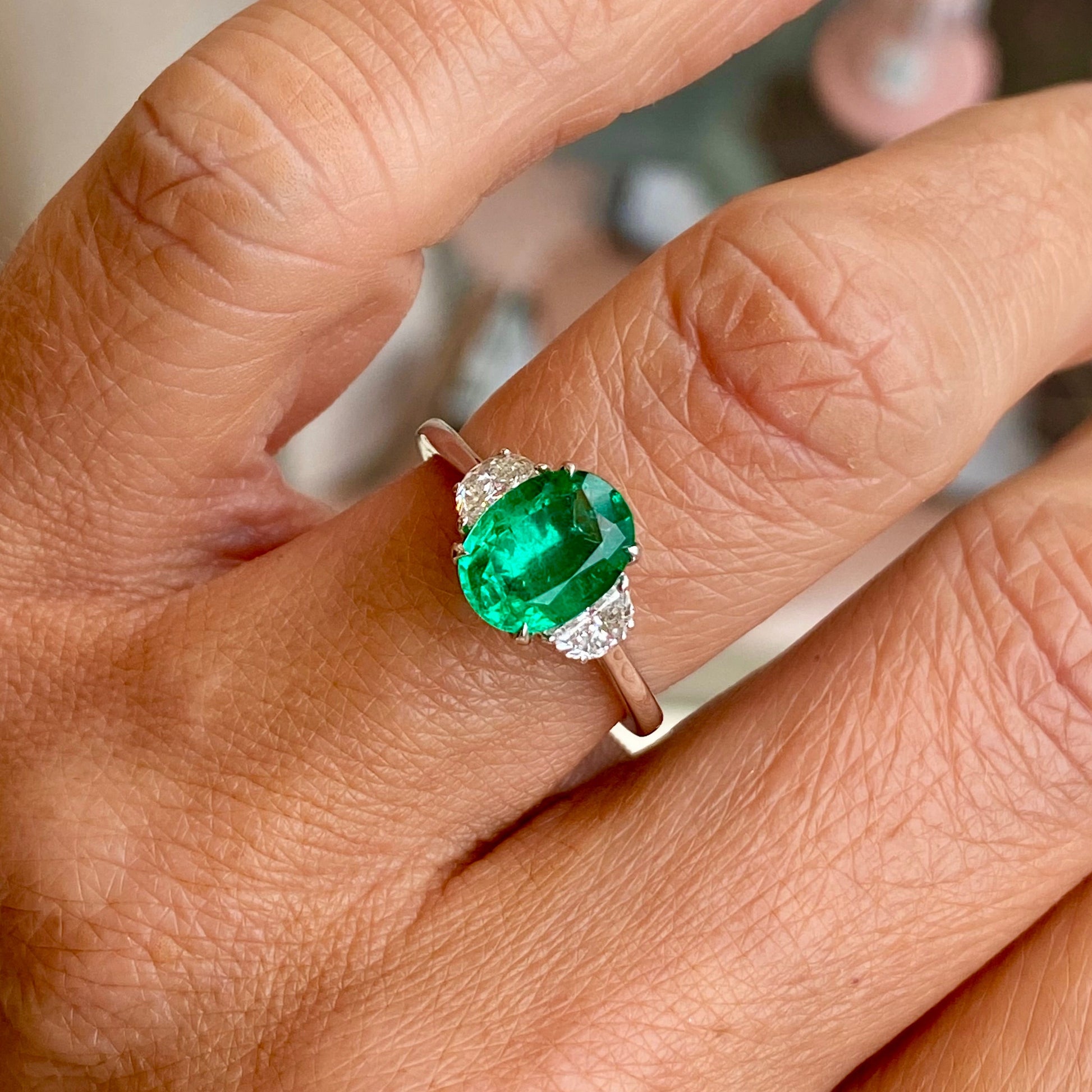 Herbert platinum emerald and diamond ring featuring a central emerald gemstone surrounded by sparkling diamonds.