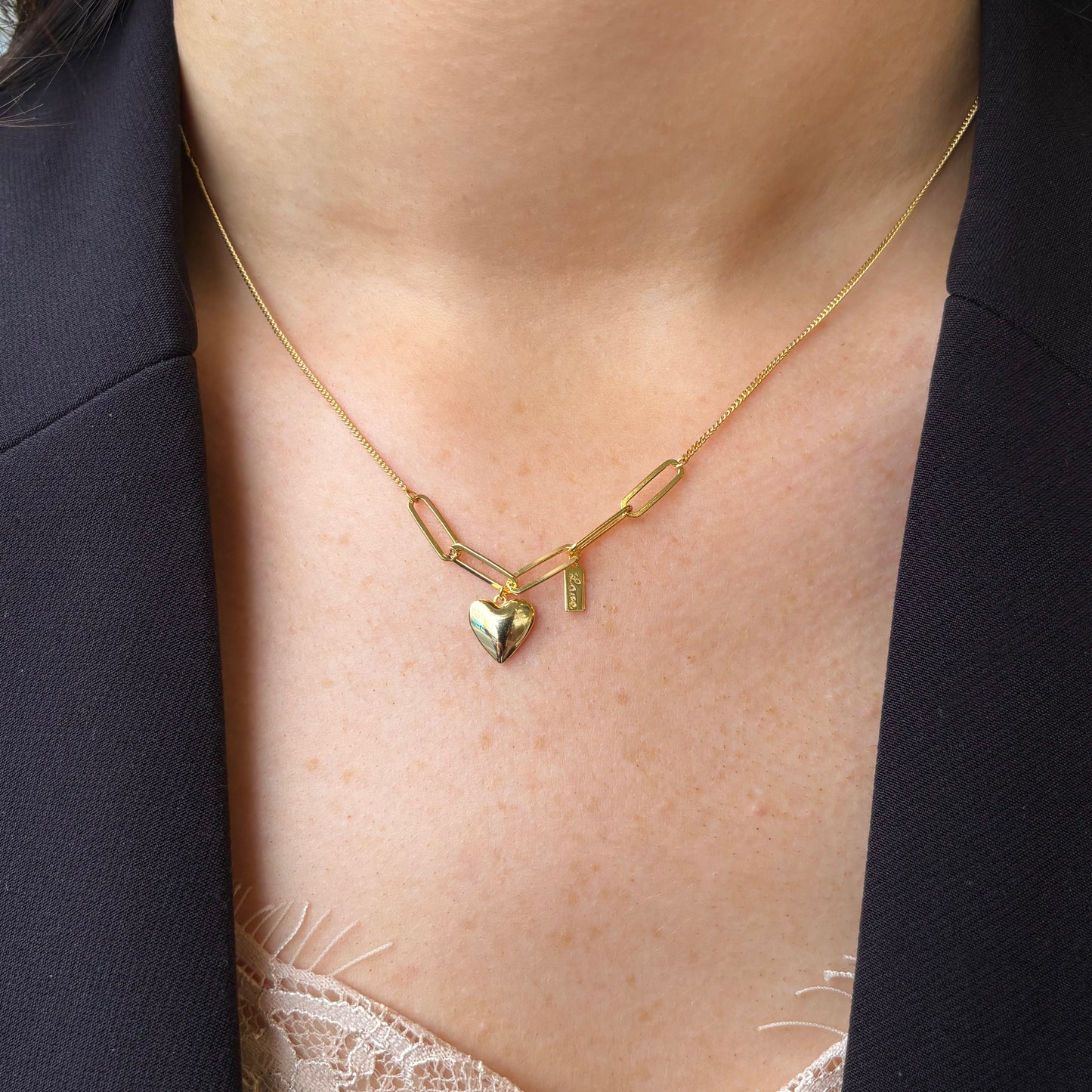 Gold necklace featuring a puffed heart and love charm, designed by Comero, with delicate chain and detailed pendant.
