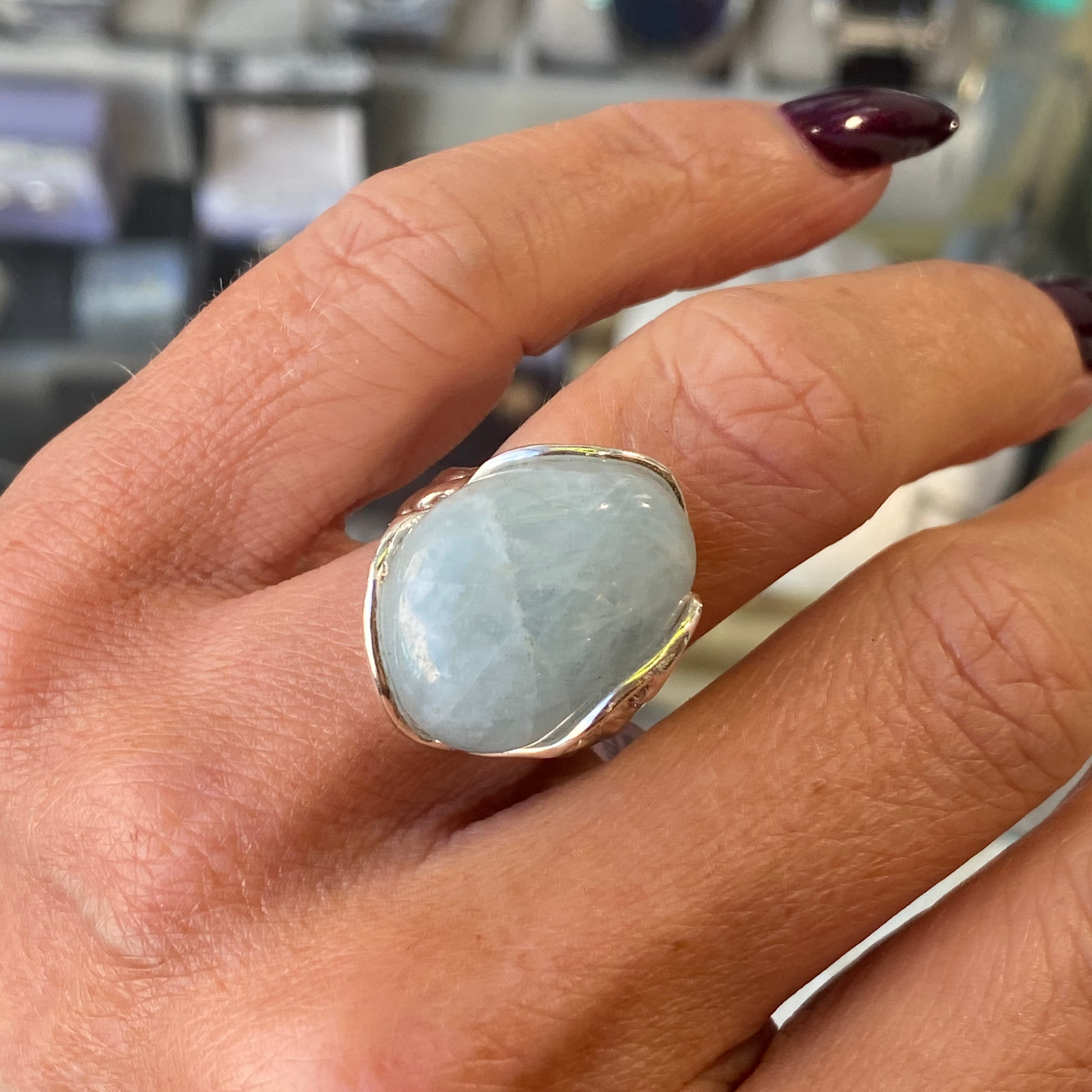 Hand wearing a ring with a large aquamarine stone against a blurred background