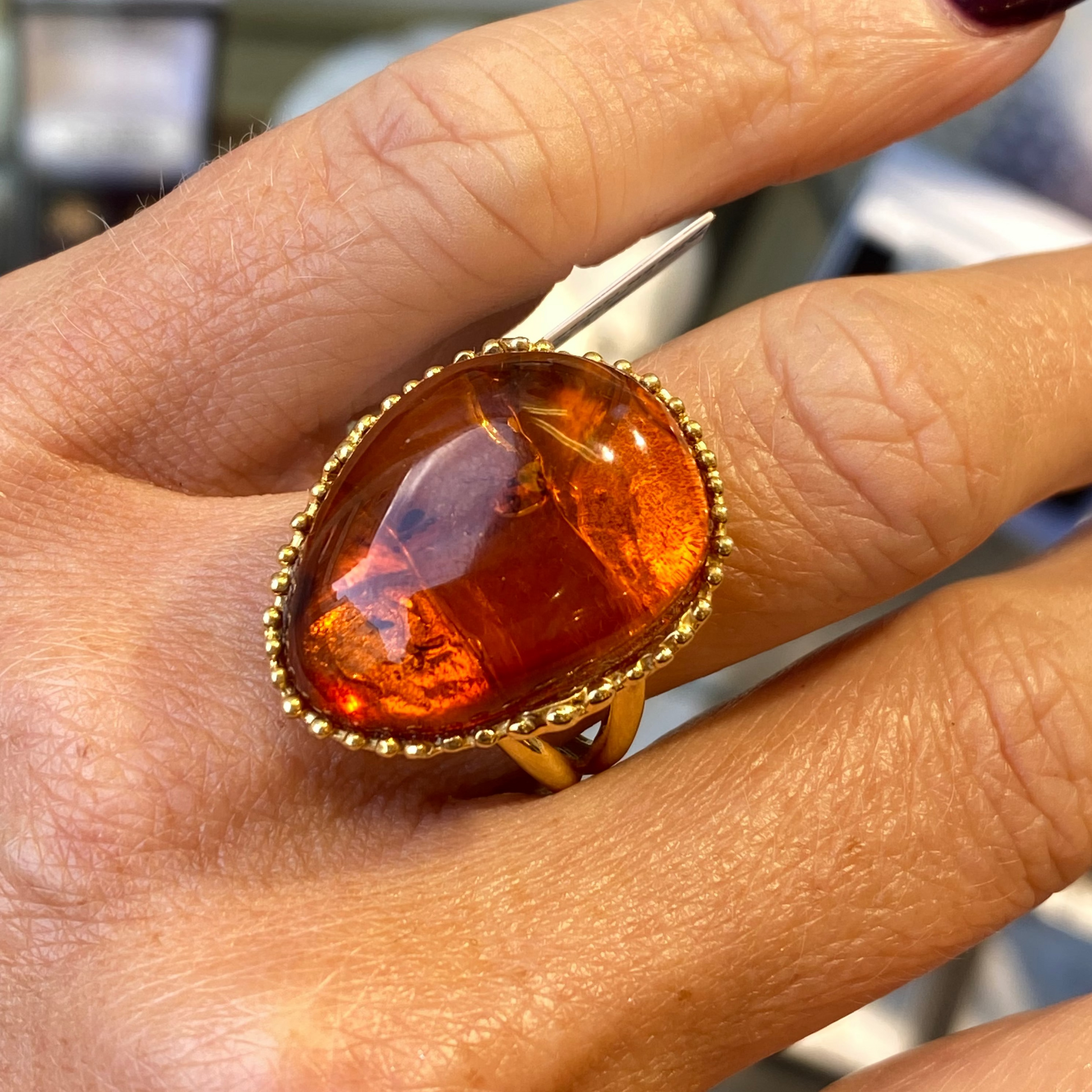 Hand wearing a ring with an amber stone on a gold band.