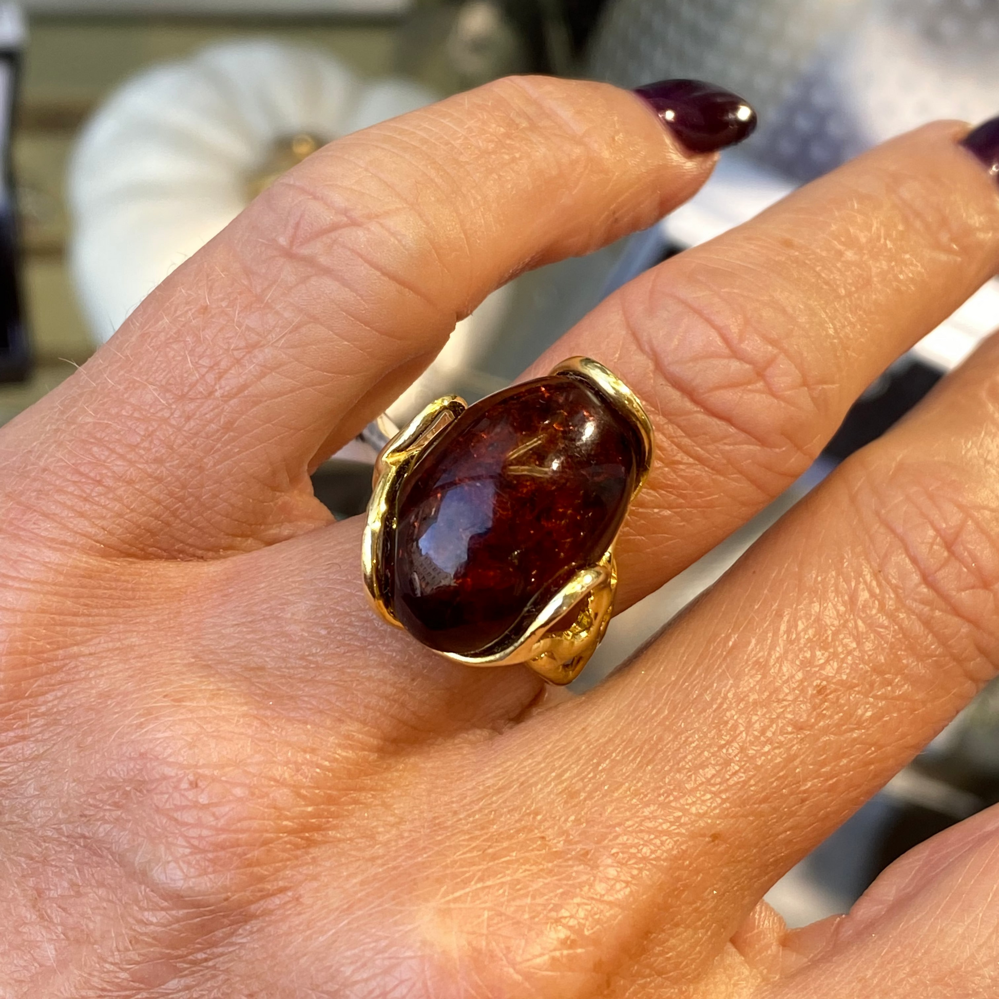Gold ring with a large amber stone on a hand against a blurred background