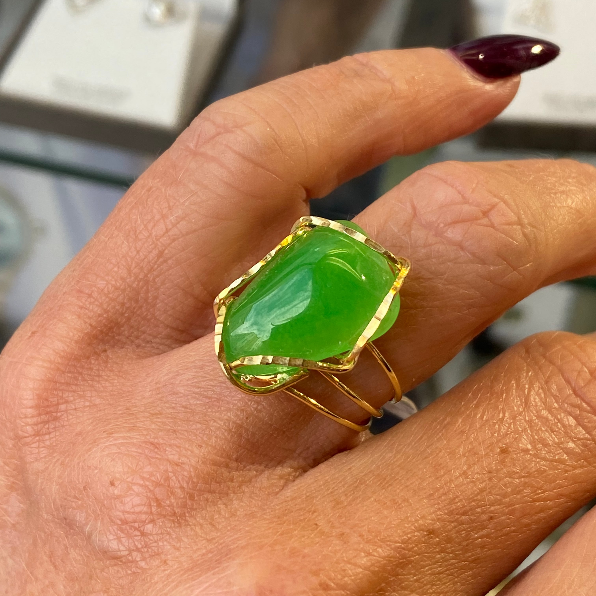 Hand wearing a jade green ring with gold band on a blurred background
