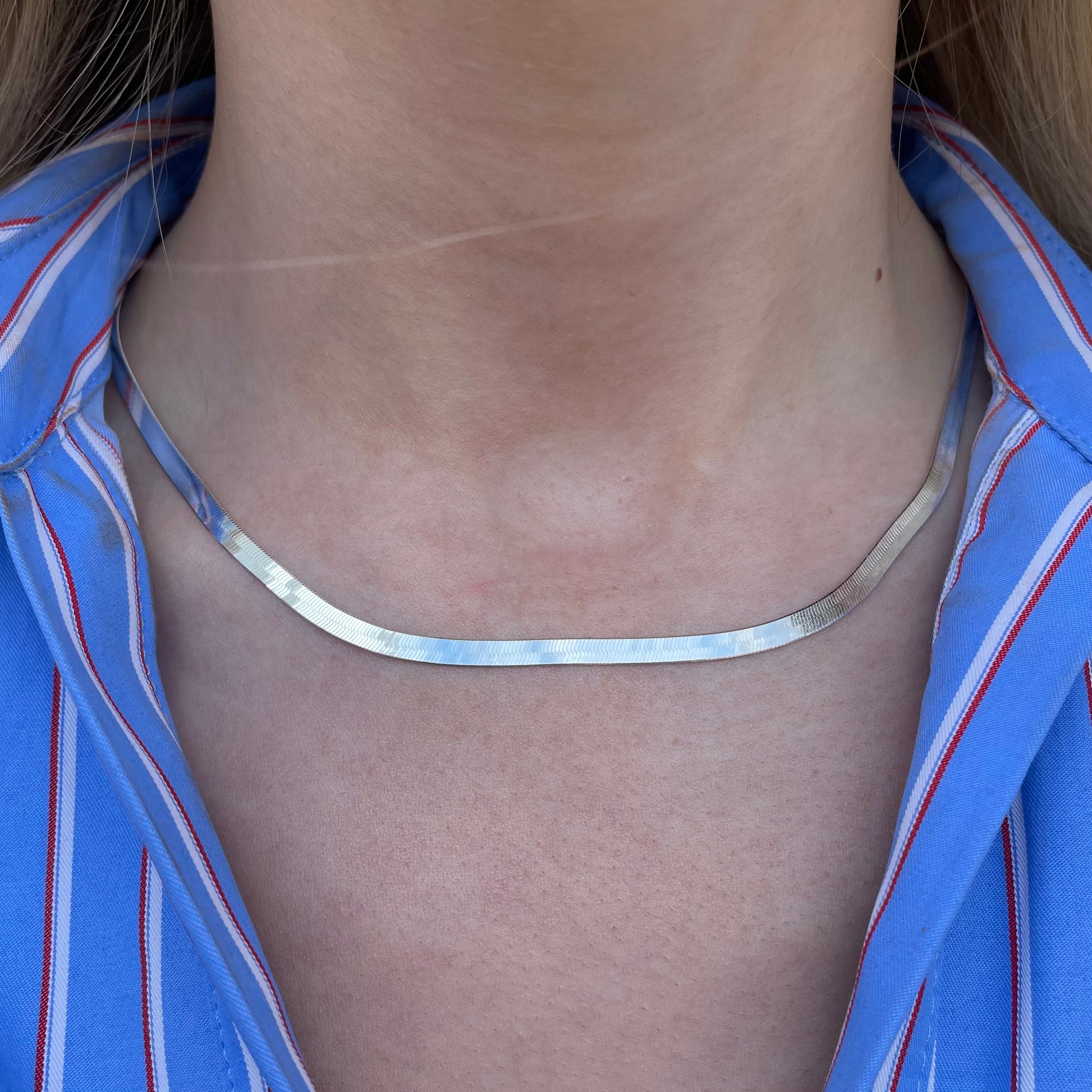 Silver necklace on a person wearing a blue striped shirt