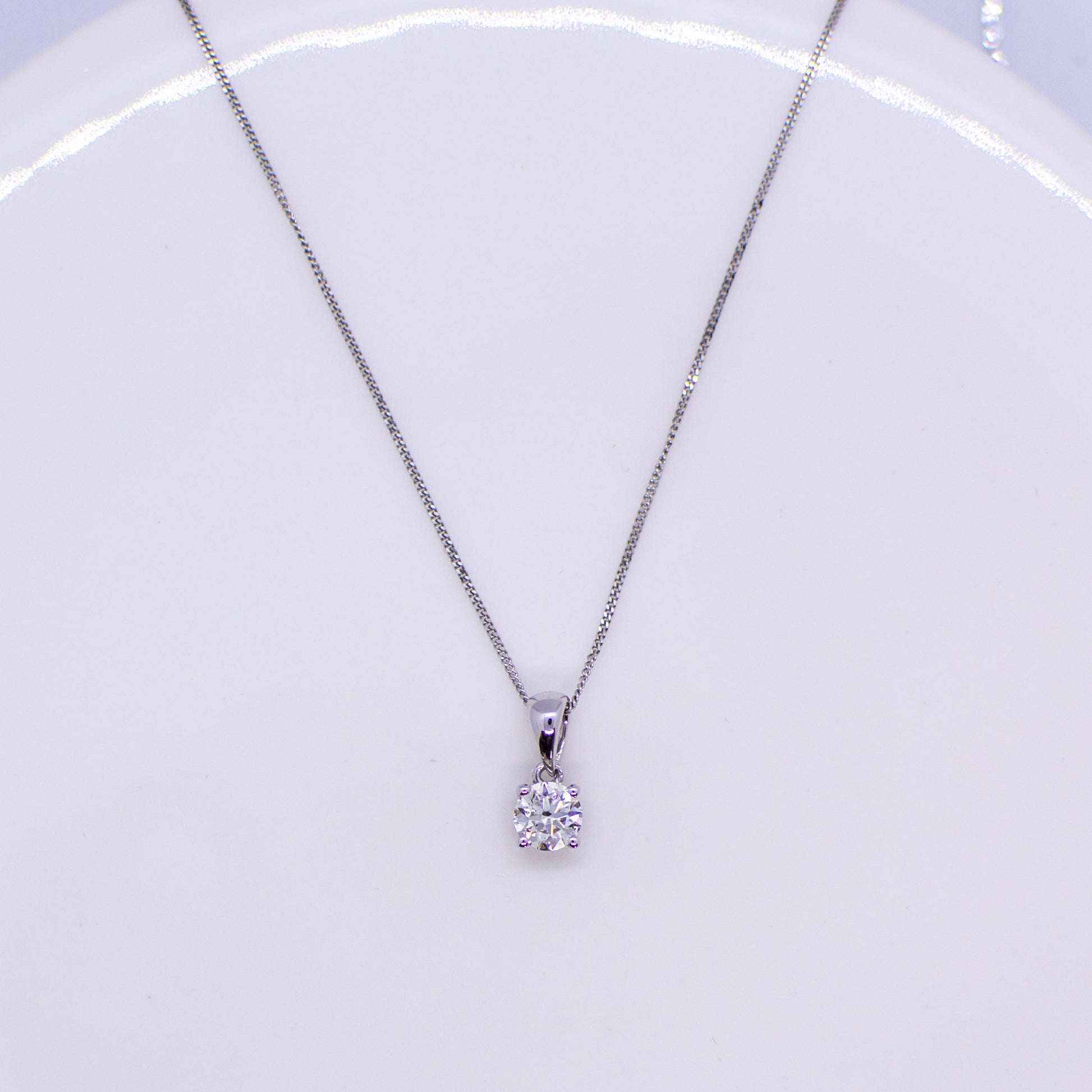 This delicate necklace comprises a single round brilliant cut diamond, in an 18ct white gold four claw setting and a 44cm long 18ct white gold fine curb chain with bolt ring clasp.