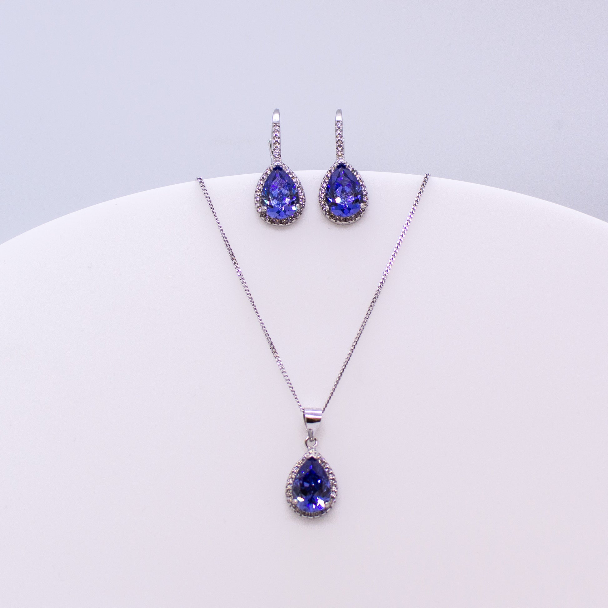 These sterling silver pear shaped drop earrings set with glittering cubic zirconia stones in created Tanzanite and white accompanied by the matching necklace are the perfect addition to any outfit. Product details: Product materials: 925 sterling silver, cubic zirconia Chain length: 44cm inch fine diamond cut curb chain Pendant dimensions:  20mm L x 10mm W Earring dimensions:  24mm L x 10mm W Drop earrings with integrated CZ set German wires.