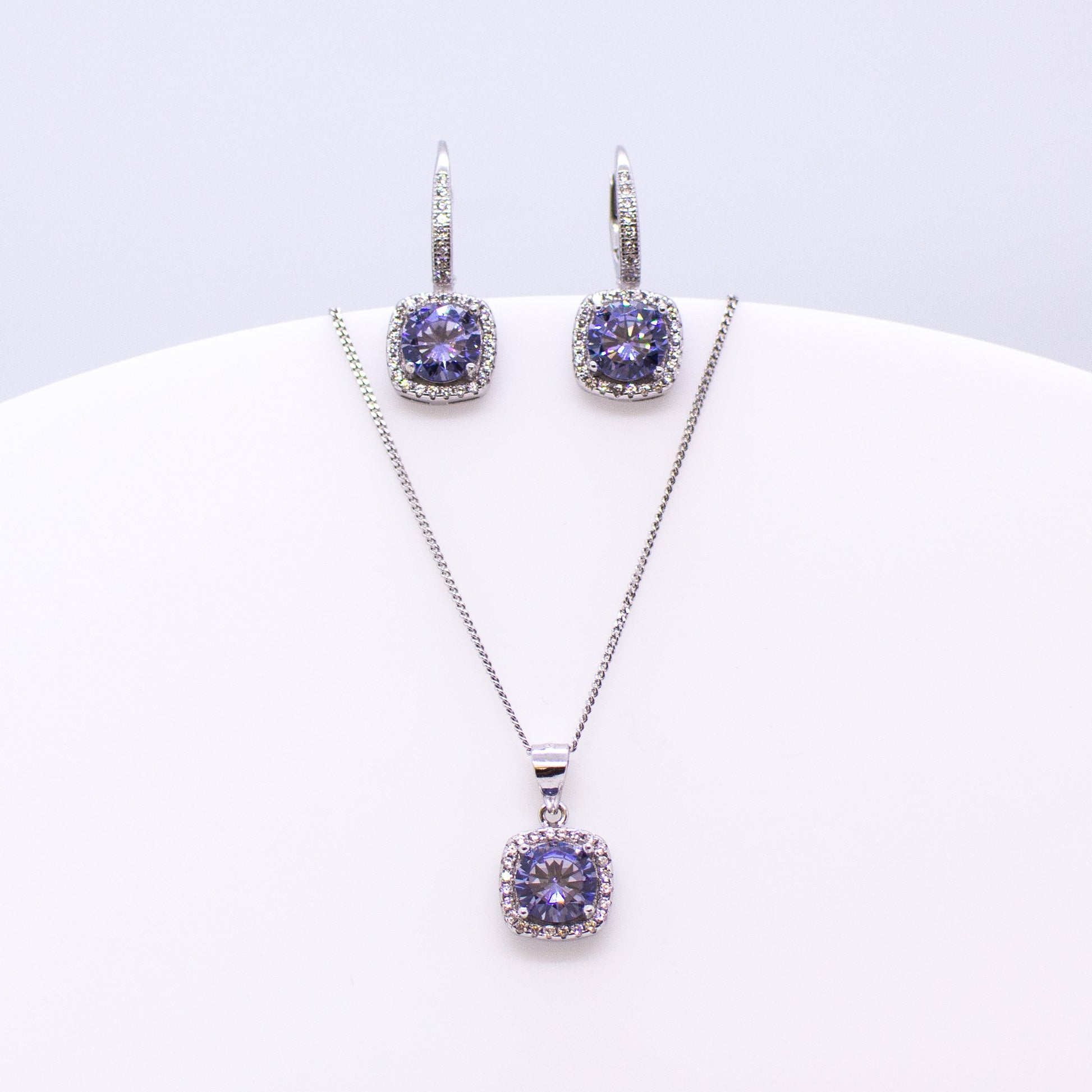 These sterling silver cushion shaped drop earrings set with glittering cubic zirconia stones in created Tanzanite colour and white accompanied by the matching necklace are the perfect addition to any outfit. Product details: Product materials: 925 sterling silver, cubic zirconia Chain length: 44cm inch fine diamond cut curb chain Pendant dimensions:  18mm L x 10mm W Earring dimensions:  22mm L x 10mm W Drop earrings with integrated CZ set German wires.