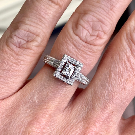 18ct White Gold Cluster Diamond Ring A single emerald cut diamond in the centre    Round brilliant cut diamonds in the halo and shoulders  A total 0.55ct of diamonds approximately  18ct white gold size M