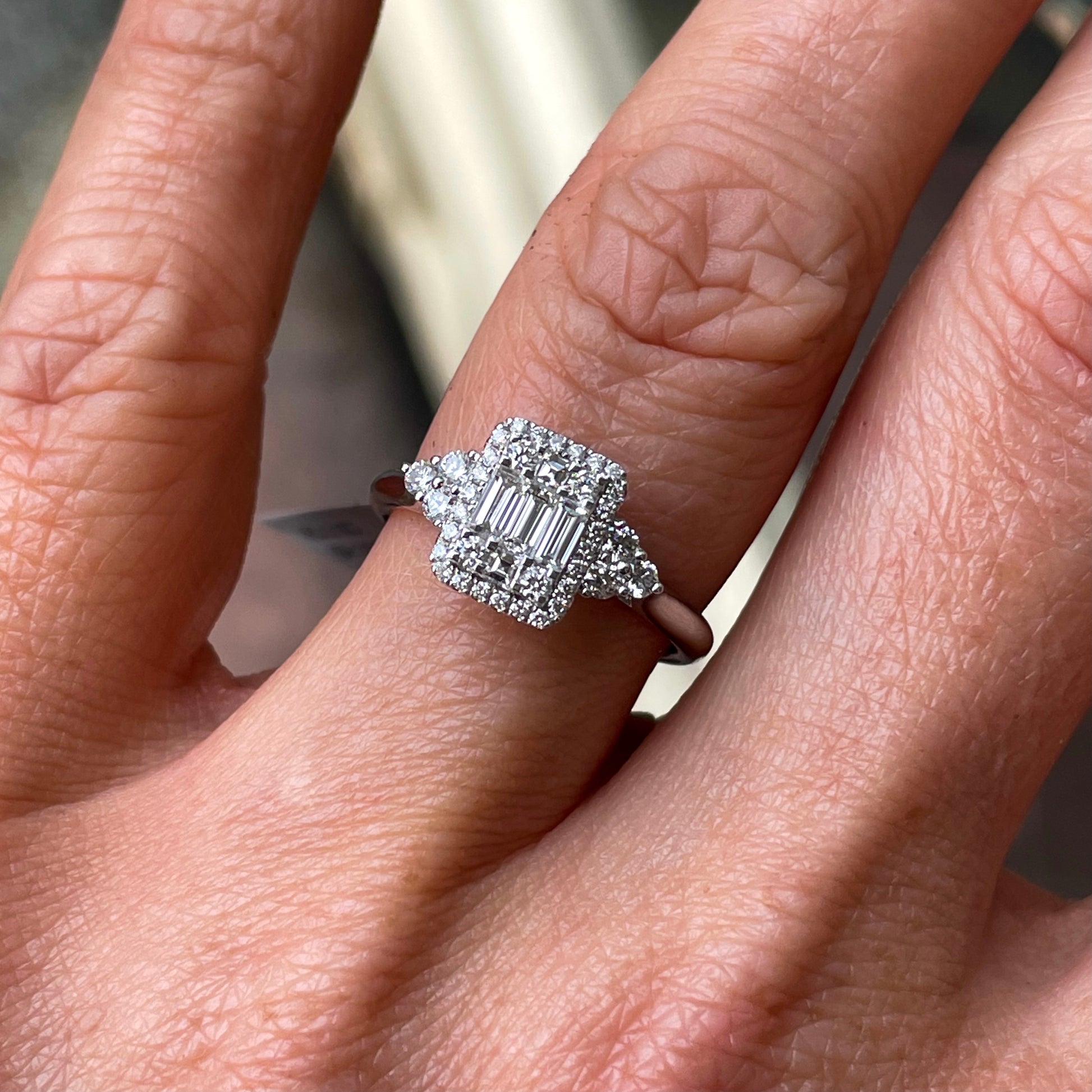 This rectangular cluster diamond engagement ring  is a complete classic.  Its simplicity is so romantic.  The Details...  One 18ct white gold diamond engagement ring.  Diamond halo cluster in a rectangular shape with trio shoulders. 0.76ct in total of diamonds, baguettes and brilliant cuts.  Colour G.  Clarity VS.  18ct white gold.  Size N.