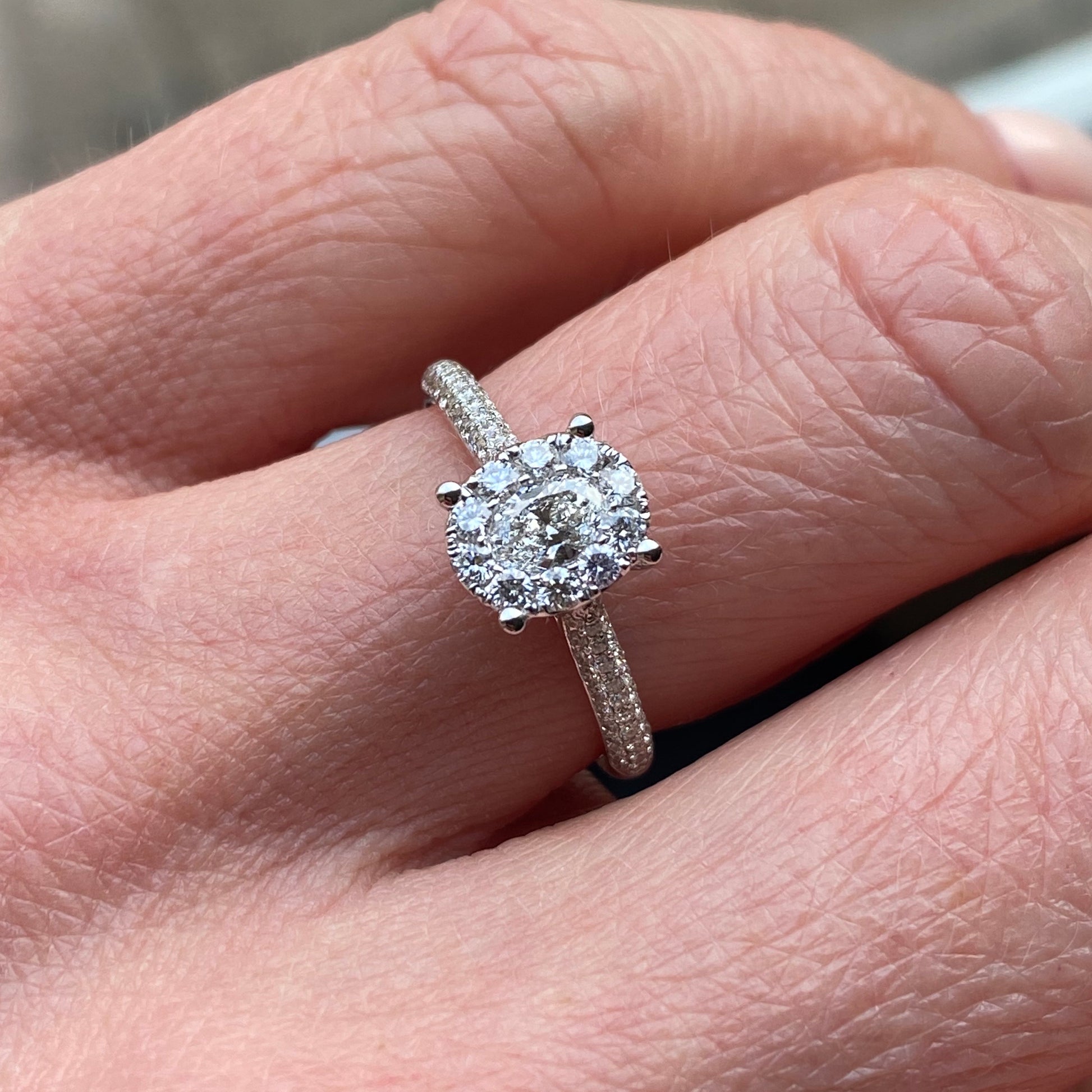 This oval cluster diamond engagement ring  is a complete classic.  Its simplicity is so romantic. The Details... One 18ct white gold diamond engagement ring.  Diamond halo cluster in an oval shape with pavé diamond-set shoulders. 0.79ct in total of diamonds.  Colour G.  Clarity VS. Centre stone: 0.23ct Melée: 0.56ct 18ct white gold.  Size N.